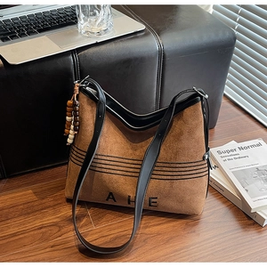 Detail of a brown suede tote bag with black trim and decorative beaded pendant on floor