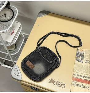 Detail of dark denim crossbody bag with woven geometric strap on industrial background