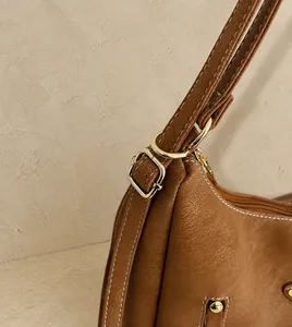Close-up of brown leather bag strap with white contrast stitching and gold metal buckle
