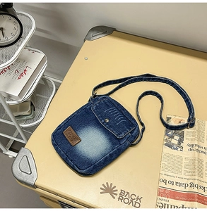 Detail of vintage blue denim crossbody bag featuring a leather logo patch and adjustable strap
