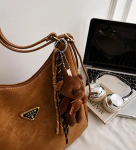Close-up of brown textured leather bag with teddy bear charm and woven rope detail