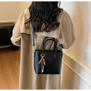 Detail of black pebbled leather bucket bag with wooden bead charm on beige trench coat
