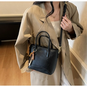 Detail of black faux leather bucket bag with retro wooden beads and gold hardware on model
