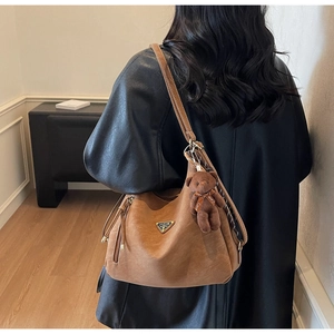 Detail of a brown leather hobo bag with metal plate and cute brown bear pendant