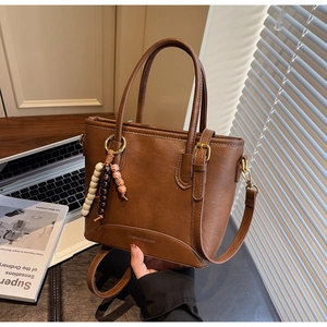 Detail of a dark brown PU leather tote bag with wooden bead charm on a wooden table