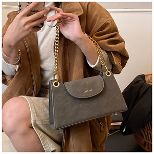 Detailed view of gray faux suede handbag with gold chain strap and branding