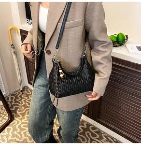 Detail shot of black woven hobo bag with wooden bead charm and slim leather strap