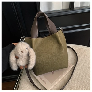 Dettaglio borsa a secchiello in pelle litchi verde scuro con manico marrone e charm coniglio