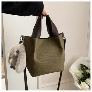 Dettaglio borsa a secchiello in pelle verde oliva con logo del brand e ciondolo a coniglio