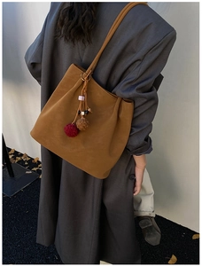 Detailweergave van bruine suède tote bag met pluche hangers op een model in herfststijl