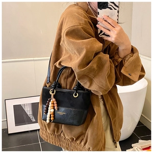Détail du sac seau en cuir noir avec empiècements en daim et perles décoratives