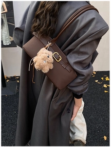 Braune Leder-Baguette-Tasche mit goldener Schnalle und Plüschhund am Model