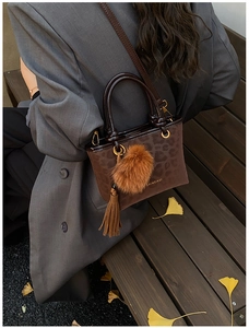 Sac seau léopard marron avec pompon porté sur un blazer gris dans une ambiance automne