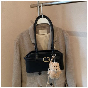 Detail der schwarzen minimalistischen Achseltasche mit goldener Schnalle und Plüsch-Anhänger
