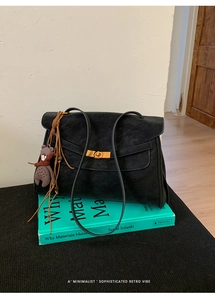 Detailansicht einer schwarzen matten Wildledertasche mit Goldverschluss und Bärenanhänger