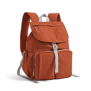 Detalle de mochila de nailon rojo óxido con solapa de hebilla y bolsillos frontales dobles