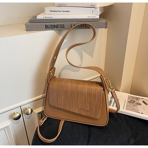 Detail of earthy leather shoulder bag featuring woven flap texture and gold metal buckle