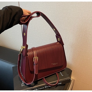 Close-up of burgundy underarm bag with woven texture flap and golden hardware accents