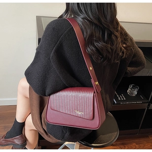 Detail of burgundy woven leather texture and golden logo on fashion shoulder bag