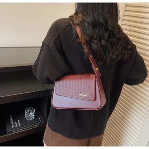 Detailed view of burgundy shoulder bag with woven texture on flap and retro design