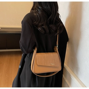 Detail of tan crossbody bag with woven texture lid and elegant gold embossed lettering