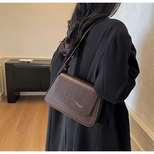 Detail view of a dark brown crossbody bag featuring a woven flap and gold brand lettering