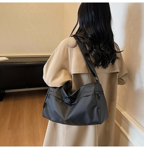 Detail of a black nylon crossbody bag with adjustable strap worn by a model in a trench coat