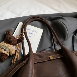 Détail d'un sac cabas en cuir marron foncé avec anses souples et charm ours mignon