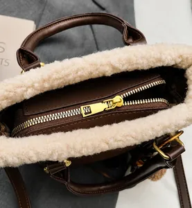 Detail shot of smooth golden zipper and cream faux fur trim on brown leather bag