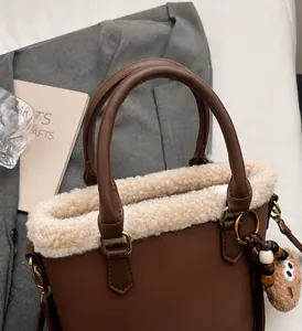 Detail of a brown leather tote with white faux fur trim and a plush bear charm on a suit