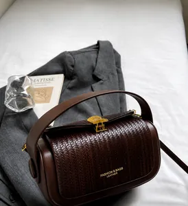 Detail of woven texture and shell-shaped golden metal clasp on a dark brown handbag