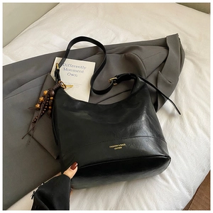 Detalle de un bolso hobo de cuero negro con correa ajustable y colgante de cuentas