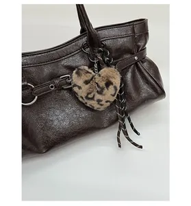 Close-up of brown textured leather handbag featuring a heart leopard plush pendant