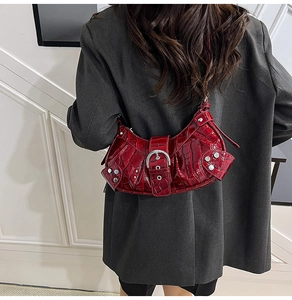 Detail of red crocodile textured crescent bag with silver rivets worn over gray blazer
