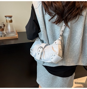 Close-up of white crocodile pattern bag featuring silver studs and adjustable strap detail