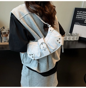 Detail of white crocodile pattern shoulder bag with silver studs and buckles worn by a model