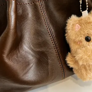Detail der dunkelbraunen Leder-Schultertasche mit Narbenstruktur und Plüschbär-Anhänger