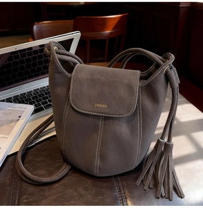 Détail du sac seau en cuir marron foncé avec pompon à franges et coutures blanches contrastées