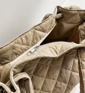 Détail de la fermeture éclair argentée et du tissu matelassé du sac beige