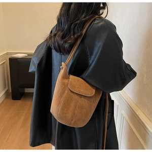 Détail du sac seau en daim marron montrant la couture délicate et le logo de mode sur le côté