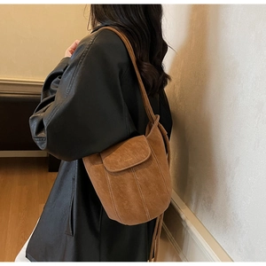 Gros plan sur un sac seau en daim marron avec surpiqûres blanches et fine bandoulière