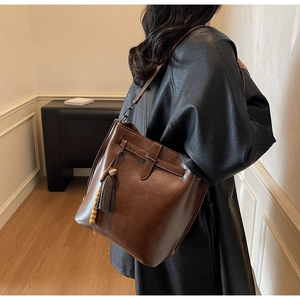 Detailansicht der dunkelbraunen Leder-Beuteltasche mit Fransenanhänger am Modell
