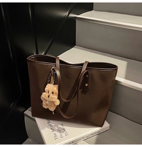 Detalle de bolso tote grande de cuero sintético marrón oscuro con colgante de perro de felpa