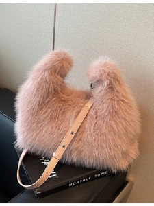 Pink plush crescent shoulder bag with leather strap and stud details on a prop box