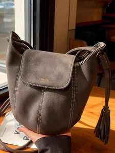 Sac seau minimaliste en cuir gris avec surpiqûres blanches et détail de pompon latéral