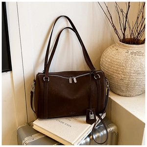 Close-up of coffee brown Boston bag with silver zipper and padlock on warm backdrop