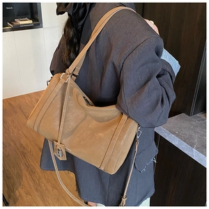 Detail of a brown suede shoulder bag showing fine stitching and a small metal padlock