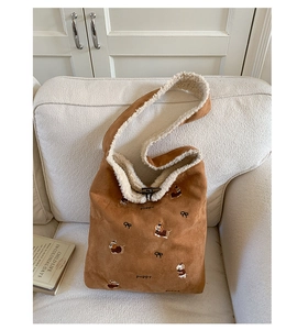 Detail of plush bucket bag with puppy embroidery and fleece lining on a white sofa