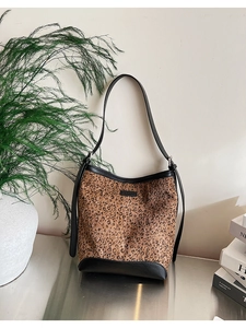 Dettaglio della borsa a secchiello leopardata con logo in pelle nera su superficie metallica
