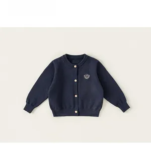 Détail du cardigan en maille bleu marine avec boutons dorés et badge de blason brodé